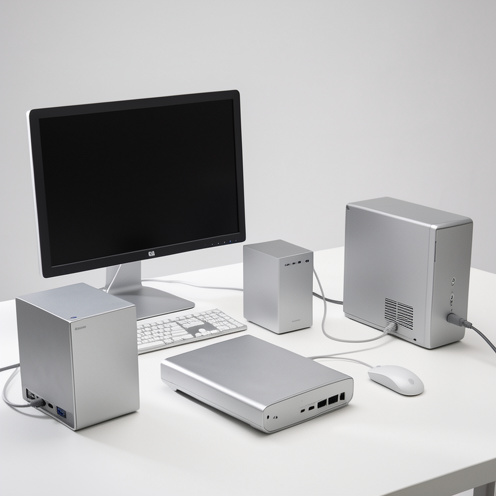 Plusieurs ordinateurs de bureau compacts en aluminium, présentés sous différents angles avec un écran, un clavier et une souris dans un studio lumineux.